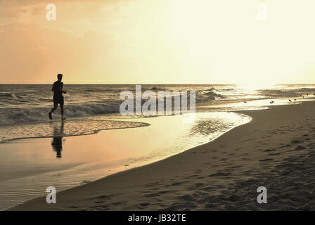 Mann läuft durch die Wellen gegen die blendende Sonne Stockfoto