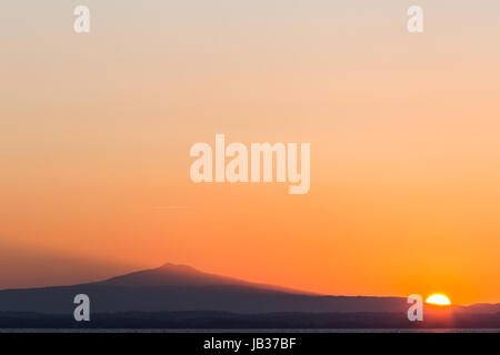 Eine minimalistische Sonnenuntergang mit Sonne in der unteren rechten Winkel, projizieren Licht in Richtung eines Berges Stockfoto