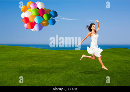 Schöne Frau laufen und springen auf einer grünen Wiese mit bunten ballons Stockfoto