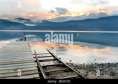 Sonnenuntergang am Okanagan Lake betrachtet aus ein altes Dock mit einer Bootsrampe neben ausgeführt. Stockfoto