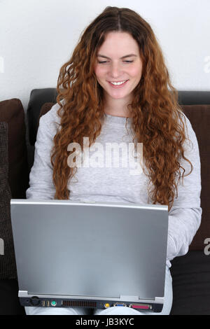 Eine Junge Frau Sitzt Mit Dachmarke Laptop-Computer Auf Dem Sofa Stockfoto