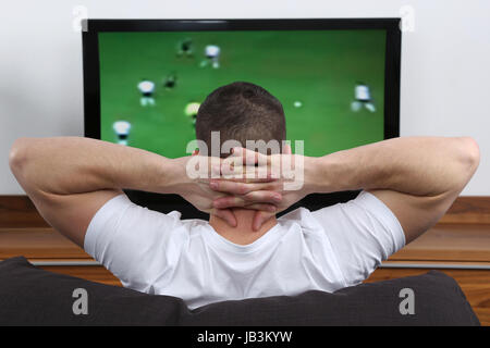 Ein Junger Mann Sitzt Auf Dem Sofa Und Schaut Fußball Im Fernsehen Stockfoto