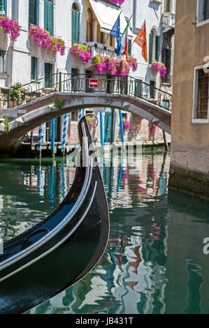 Gondel in einem Kanal mit Brücke und venezianischen, italienische und Europäische Union Flaggen im Hintergrund. Venedig, Italien. Stockfoto