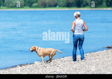 Reife Frau mit einem Labrador-Retriever am Flussufer Stockfoto