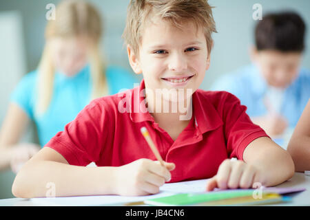 Porträt der glückliche Schüler am Arbeitsplatz Blick in die Kamera mit seinen Mitschülern auf Hintergrund Stockfoto