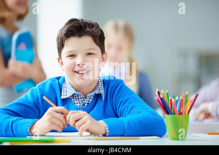 Porträt der glückliche Schüler am Arbeitsplatz Blick in die Kamera mit seinen Mitschülern auf Hintergrund Stockfoto