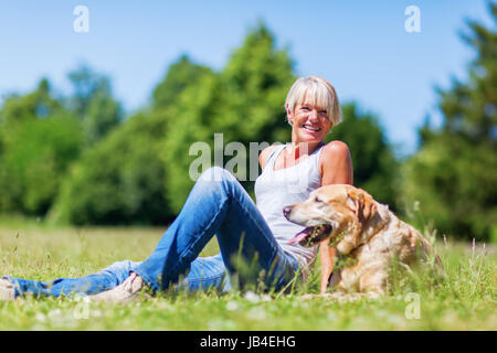 Reife Frau mit einem Labrador Retriever sitzen auf dem Rasen Stockfoto