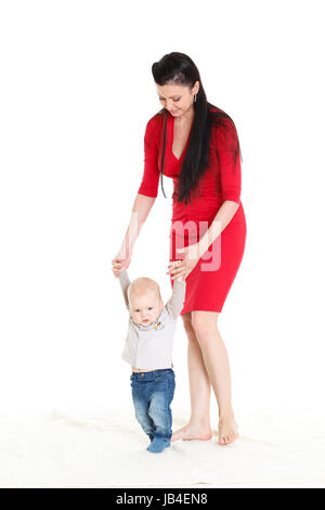 Glückliche junge Mutter hilft ihrem kleinen Sohn die ersten Schritte zu tun. Stockfoto