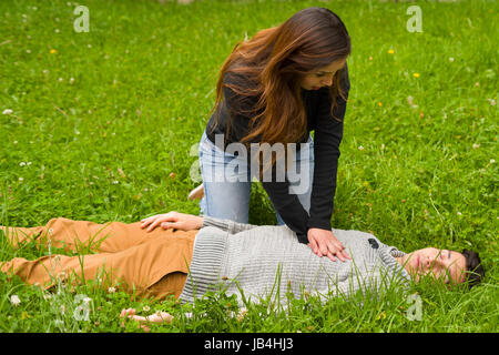 Schöne Frau, erste Hilfe, ein hübscher junger Mann, Herz-Lungen-Wiederbelebung, in einem Rasen Hintergrund geben. Stockfoto