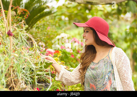 Fröhliche junge Frau, die im Freien im Garten trägt einen roten Hut im Garten Hintergrund stehen. Stockfoto