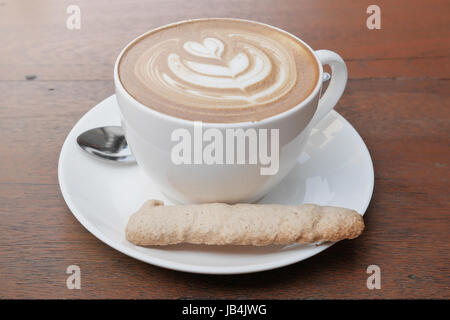 Latte Art Kaffee mit Herz Muster in eine weiße Tasse und Cookie auf hölzernen Hintergrund Stockfoto