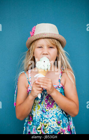 Niedliche junge Mädchen essen Vanilleeis in Kegel außerhalb Hintergrund blaue Wand Stockfoto