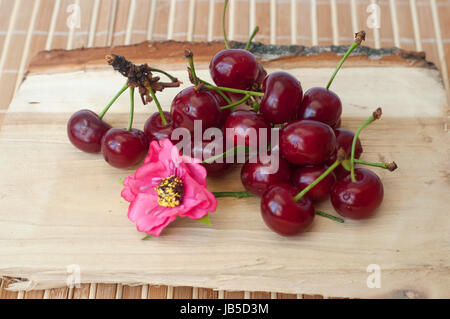 Schließen Sie sich frisch und appetitlich Kirschen auf ein Stück Holz auf dem beigen Hintergrund isoliert Stockfoto