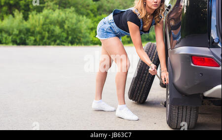 Frau ändert sich das Rad des Autos auf einer Straße Stockfoto