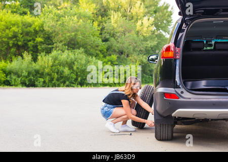 Frau ändert sich das Rad des Autos auf einer Straße Stockfoto