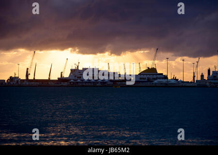 Die kommerzielle Seehafen mit großen Schiffe und Kräne bei Sonnenuntergang mit dramatische Wolken am Himmel, Bari, Italien Stockfoto