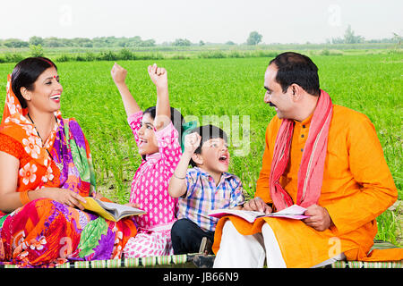 Happy Indischen ländlichen Bauern Familie - Eltern und 2 Kinder studieren Bücher helfen Bildung in Feld Stockfoto