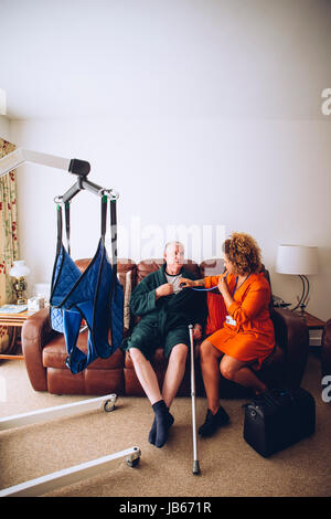 Homecare Krankenschwester Überprüfung eines älteren Mannes mit einem Stethoskop in seinem Haus. Es ist ein Hebezeug eingerichtet. Stockfoto