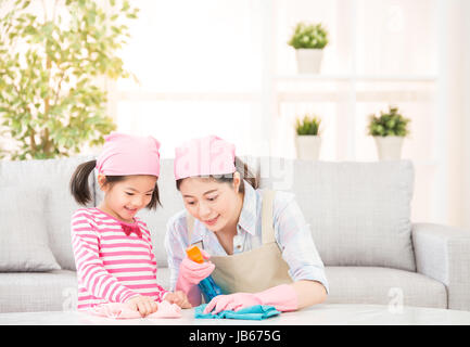 Glückliche Familie reinigt das Wohnzimmer. Mutter und Tochter machen die Reinigung im Haus. Eine junge Frau und ein kleines Kind Mädchen abstauben. Familie Hausarbeit Stockfoto