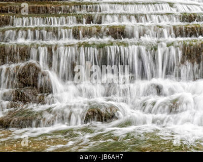 Nahaufnahme eines Wasserfalls erstellt von Flusswasser über eine Reihe von niedrigen Steinstufen, an der Unterseite, wie es in großen und kleinen Steinen fließt in Strömen. Stockfoto