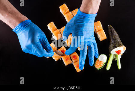 7/8-Ansicht von Küchenchef bereitet Sushi auf schwarzem Hintergrund Stockfoto