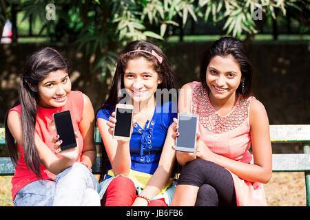 Indische Teeanger Mädchen Freunde anzeigen Handy Bildschirm in Park Stockfoto