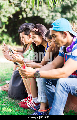 Indische Gruppe College Freunde zusammen sitzt im Park und Messaging auf Telefon Stockfoto