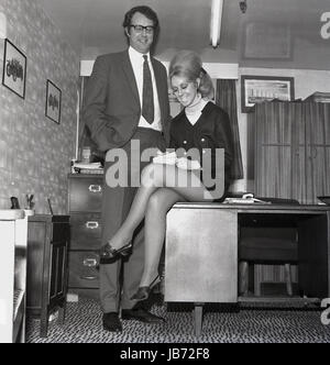 1970er-Jahren, historische, sitzt eine Sekretärin, ein Mini-Hemd trägt am Rande der Schreibtisch, wie sie Notizen von ihrem Chef in seinem Büro kuppelt. Stockfoto