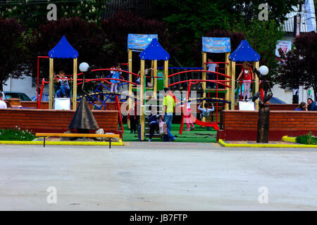 Bunte Kinder-Spielplätze in einem öffentlichen Park, umgeben von grünen Bäumen bei Sonnenuntergang. Das Konzept der Kindheit in den Städten. Stockfoto