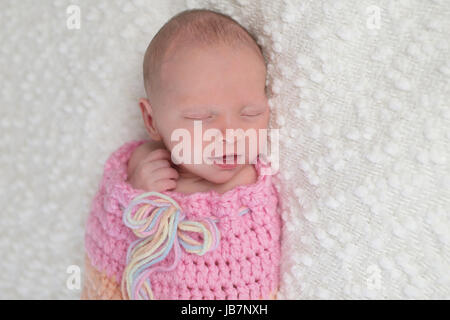 Kopfschuss von einem lächelnden drei Wochen alten neugeborenen Mädchen gebündelt in einem hellrosa, gehäkelt, kuscheln Sack. Sie liegt auf einer weißen, Bouncle Decke. Stockfoto