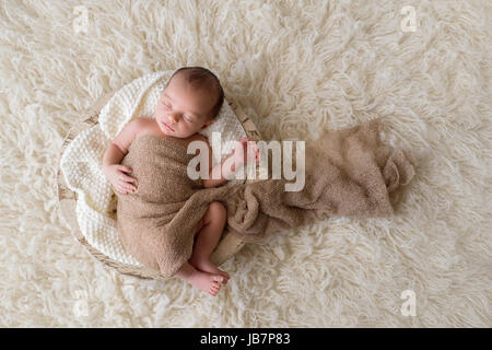 Zwei Wochen altes neugeborenes Baby junge gepuckt in Beige wickeln und schlafen in einer runden, hölzernen, Graben-Schüssel. Gedreht im Studio auf einem Creme farbigen Flokati ru Stockfoto