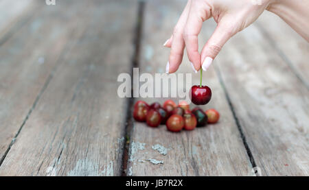 Eine weibliche Hand ist die Auswahl einer Kirsche von einer hölzernen Tisch. Stockfoto