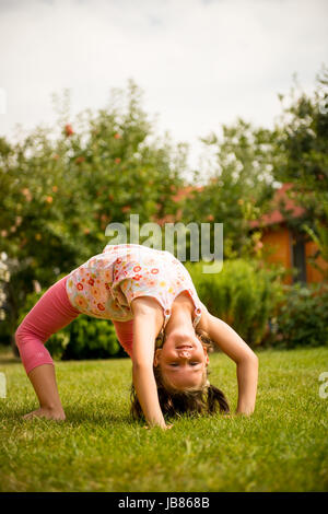 Sport auf Rasen - lächelnd kleines Kind machen Brücke im Freien im Garten Stockfoto