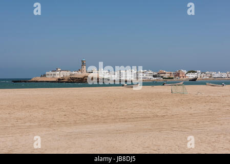 Ein Strand mit weichem Sand im Vordergrund und der historische Leuchtturm Al Ayjah in Sur, Sultanat Oman, Reiseziel auf der Arabischen Halbinsel Stockfoto