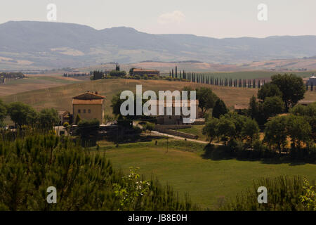 VAL D'ORCIA, Italien - 3. Juni 2017: Hills Val D'orcia-Umgebung in der Region Toskana in Italien, mit Häusern und Zypresse im Hintergrund Stockfoto