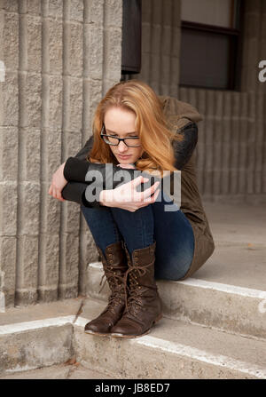 Outdoor-Foto junge Teenager-Mädchen sitzen auf konkrete Schritte, Knie, verzweifelten Gesichtsausdruck umarmt. Stockfoto