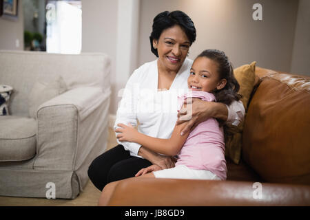 Porträt der Großmutter und Enkelin beim Sitzen auf dem Sofa zu Hause umarmt Stockfoto