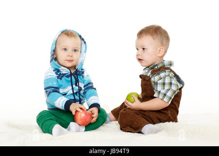 Zwei kleine Jungs mit frischen Äpfeln sitzen auf einem weißen Hintergrund. Gesunde Ernährung. Stockfoto
