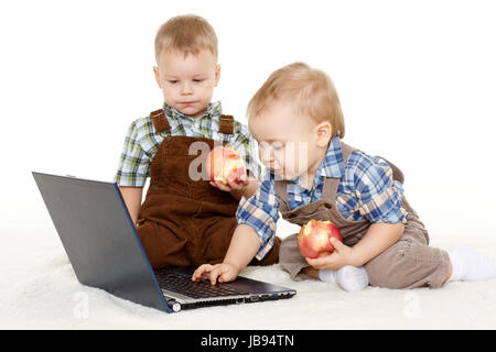 Zwei kleine Jungs mit Notebook und frische Äpfel sitzen auf einer Etage auf einem weißen Hintergrund. Stockfoto
