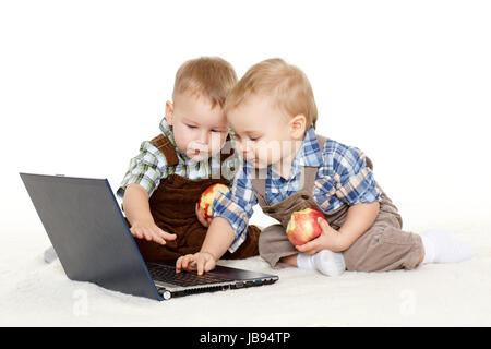 Zwei kleine Jungs mit Notebook und frische Äpfel sitzen auf einer Etage auf einem weißen Hintergrund. Stockfoto