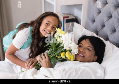 Hohen Winkel Porträt von lächelnden Großmutter und Enkelin mit Blumenstrauß auf Bett zu Hause Stockfoto