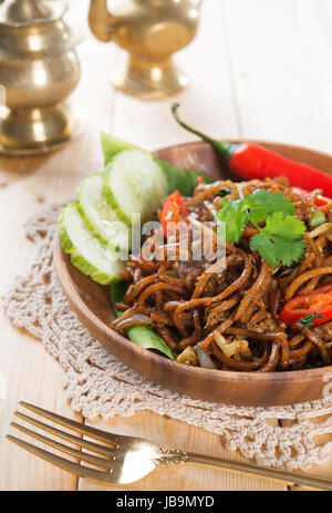 Würzig gebratene Nudeln. Indonesischen und malaysischen Küche, mi Goreng oder mich Goreng Mamak mit Esstisch aus Holz. Frisch heiß mit gedünstetem Rauch. Stockfoto