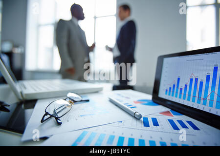 Bild von Brillen, Stift, Touchpad und Finanzdokumente am Arbeitsplatz mit Geschäftsleuten, die Kommunikation auf Hintergrund Stockfoto