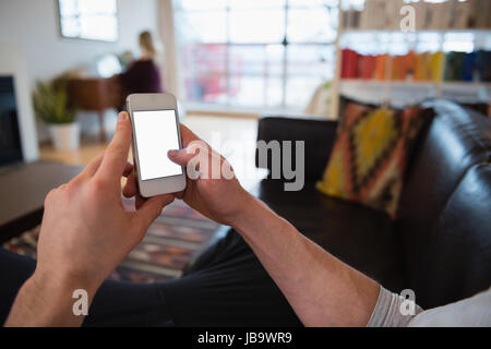 Händen eines Mannes mit Handy im Wohnzimmer zu Hause Stockfoto
