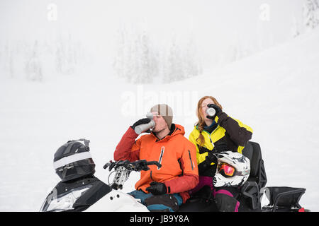 Paar beim Kaffee aus Thermoskanne beim Entspannen in Motorschlitten im winter Stockfoto