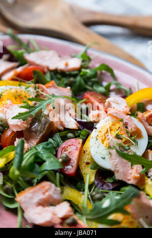 Salat mit Lachs, Gemüse und Grün in rosa Platte auf Retro-Zeitung Hintergrund Stockfoto