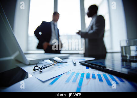 Brille, Glas Wasser, Stift, Laptop, Touchpads und Finanzdokumente am Arbeitsplatz mit Geschäftsleuten, die Kommunikation auf Hintergrund Bild Stockfoto