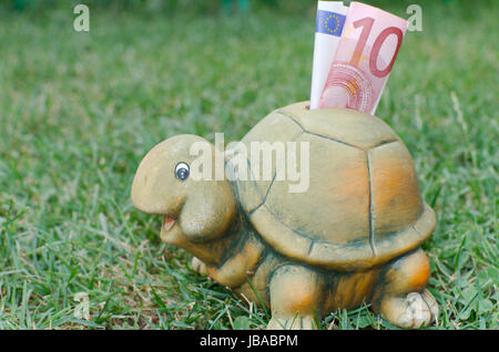 Glückliche Schildkröte Sparschwein mit zehn Euro-Banknote in dem grünen Rasen Stockfoto