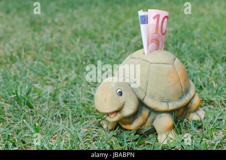Glückliche Schildkröte Sparschwein mit zehn Euro-Banknote in dem grünen Rasen Stockfoto