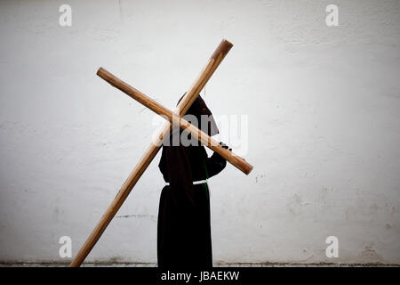 Eine vermummte Büßer trägt ein Kreuz während der Karwoche in Baeza, Provinz Jaen, Andalusien, Spanien Stockfoto